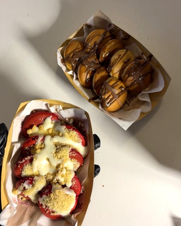 Two trays of mini pancakes, one with white drizzle and crumbs, one with chocolate drizzle