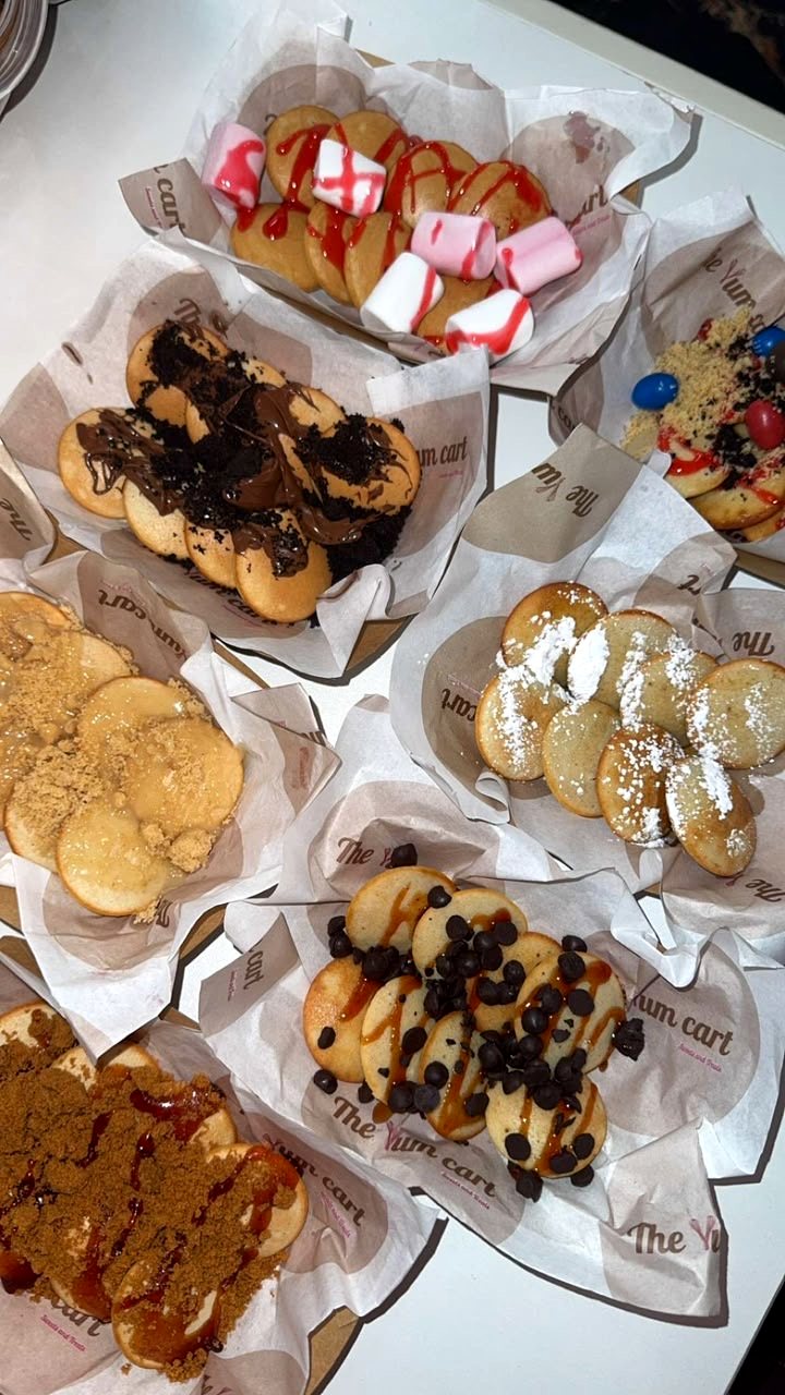 Seven trays of mini pancakes with different toppings and drizzles